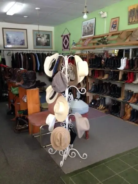 An interior view of a store displaying hats on a rack and boots on shelves.