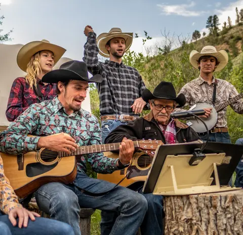 A group of people in cowboy hats play and sing music outdoors.