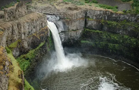 A waterfall plunges into a rocky canyon basin surrounded by cliffs.
