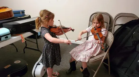 Two young girls practice playing violins indoors.
