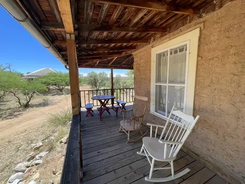 A rustic porch with rocking chairs and a table overlooks a dry landscape under a clear sky.