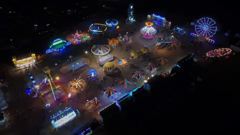 An aerial nighttime view of an illuminated carnival with various rides.