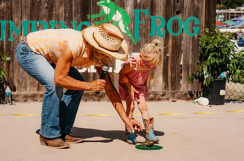 A woman holding a microphone and a young child look down at a frog on the ground.