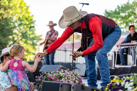 A country musician in a cowboy hat bends down to interact with a young child during a performance.