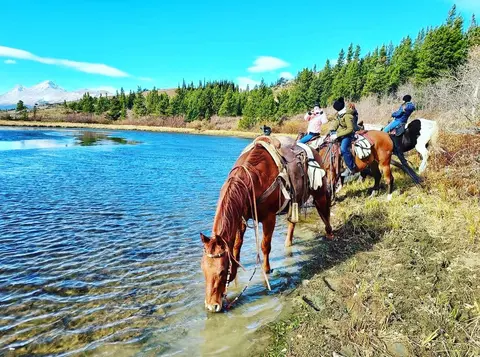 People ride horses by a lake in a scenic landscape.