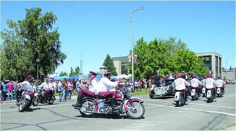 A group of people in matching uniforms ride motorcycles down a street during an event.