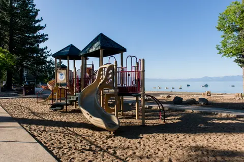A playground sits on a sandy beach near a large lake.