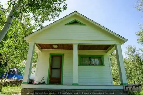 An exterior view of a small white house with green trim and a front porch.