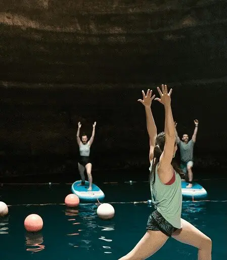 People doing paddleboard yoga in a cavern with water.