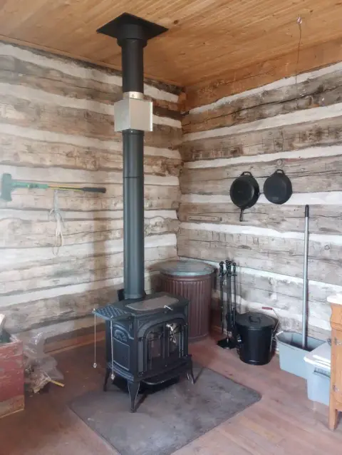 A black wood-burning stove sits in the corner of a rustic log cabin interior.