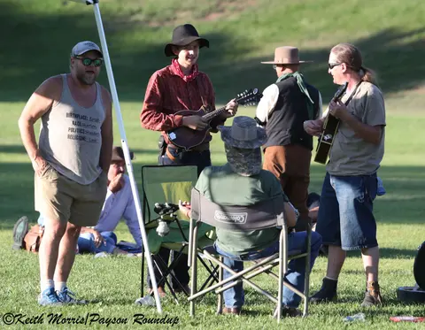 Several people gather outdoors on grass playing musical instruments.