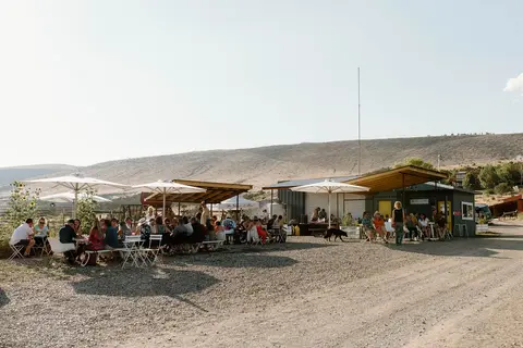 People gathered at outdoor tables and umbrellas near a building.