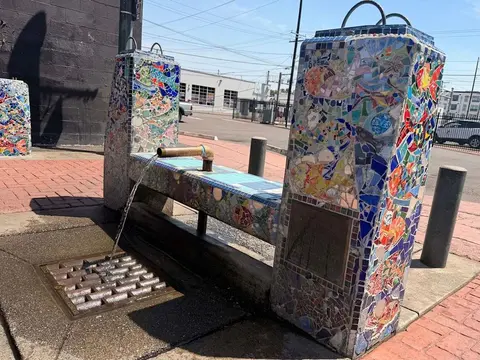 A colorful mosaic water fountain stands outdoors on a sidewalk.