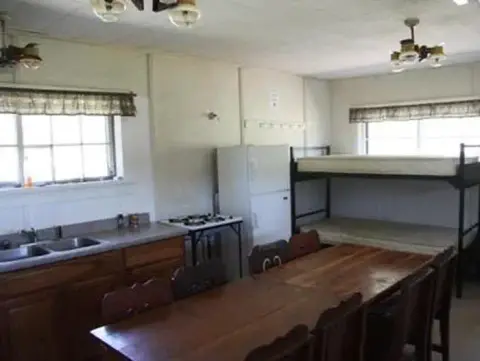 An interior view of a room with a kitchen area, dining table, and bunk bed.