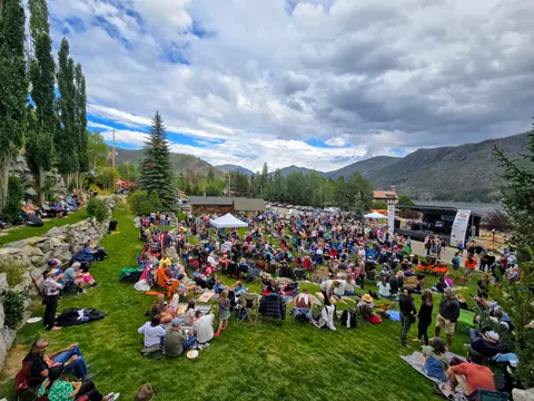 A large crowd gathers on a grassy hillside for an outdoor event.
