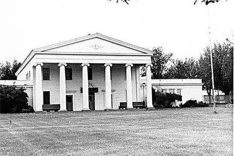 A historic black and white photo shows the exterior of a classical building with large columns.