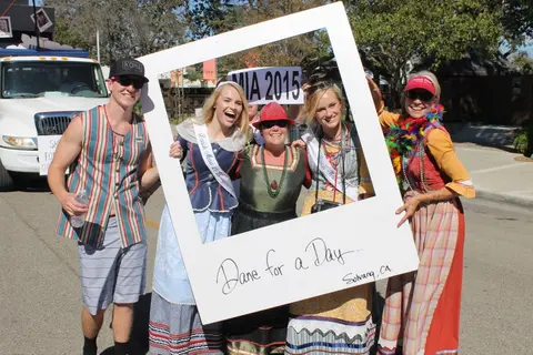 A group of people pose behind a large picture frame outdoors.