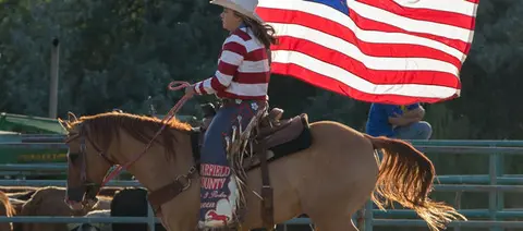 A person rides a horse while carrying an American flag.