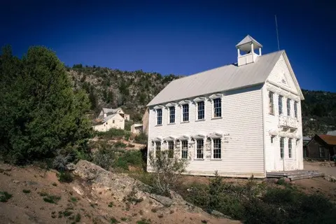 A historic two-story white building stands in a desert landscape with mountains in the background.
