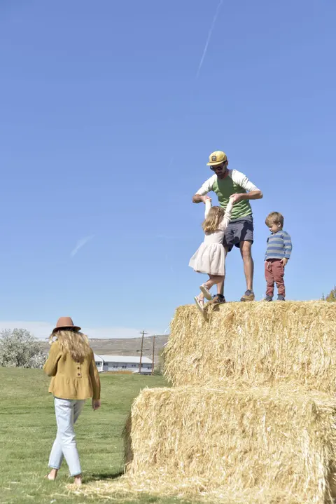 A family playing near large hay bales under a clear sky.
