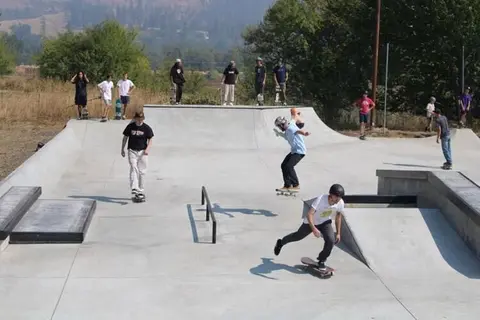People skateboarding at an outdoor concrete skatepark.
