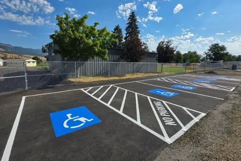 A newly paved parking lot features several painted handicap parking spaces and a chain-link fence outdoors.