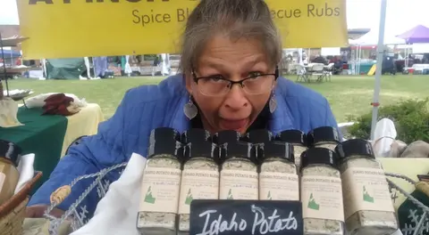 A woman poses behind a display of spice blends at an outdoor market.