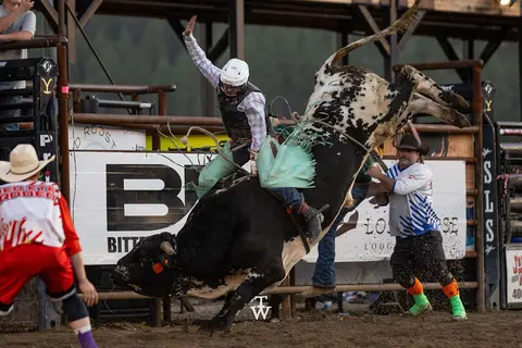 A cowboy rides a bucking bull in an arena.