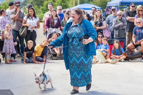 A smiling woman walks her small dog on a leash in front of a crowd of spectators.