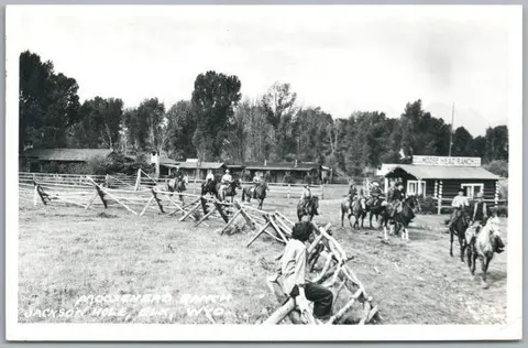 A black and white photograph showing people on horseback at a ranch.