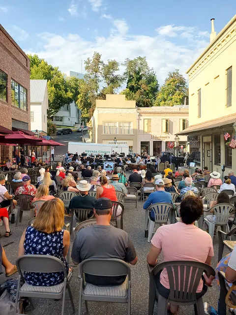 A crowd of people seated outdoors listening to a band performing in a city street.
