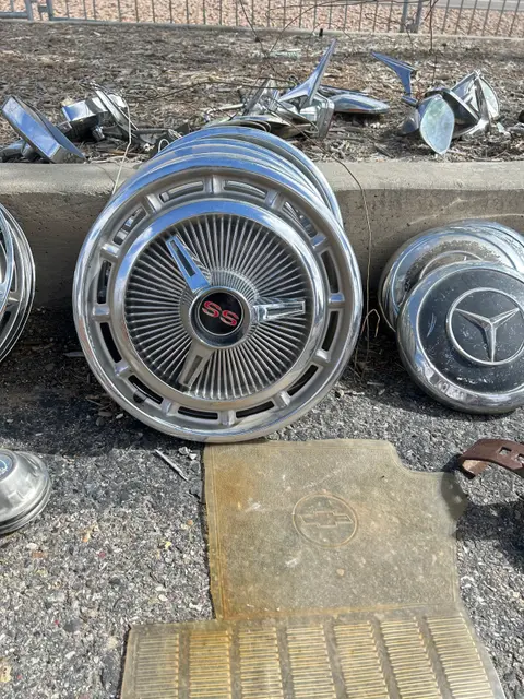 A stack of chrome hubcaps and a rubber car mat resting on asphalt.