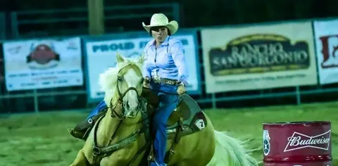 A woman rides a horse around a barrel in an arena.
