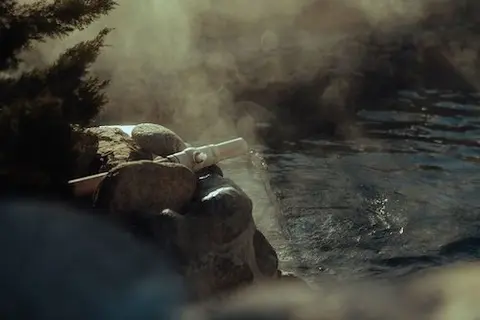 Water flows from a pipe into a hot spring pool with steam rising.