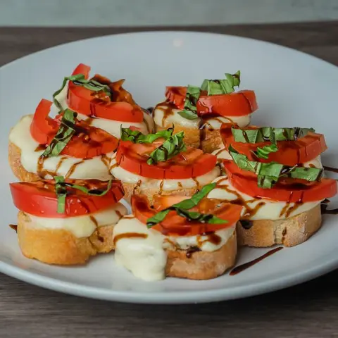 A plate of bruschetta topped with cheese, tomatoes, basil, and balsamic glaze.