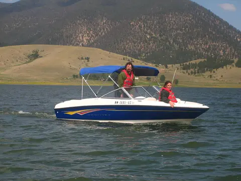 Two people ride in a motorboat on a lake with mountains in the background.