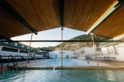 An outdoor swimming pool surrounded by buildings with a covered seating area in the foreground.