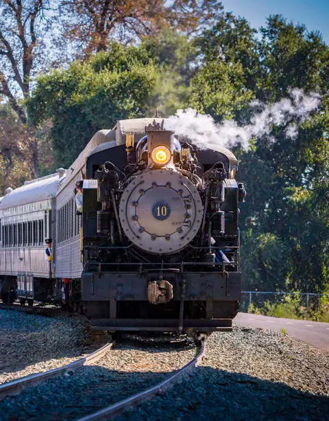A steam locomotive pulling passenger cars along tracks.