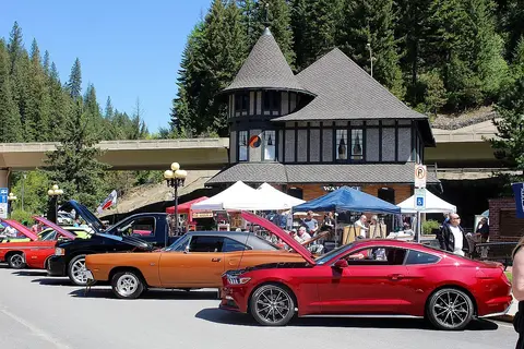 Classic and modern cars parked in front of a historic building with tents and people nearby.