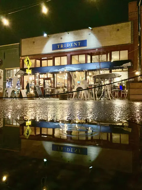 An exterior view of a storefront at night with a reflection in a puddle.