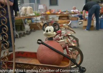 A vintage Mickey Mouse toy rests inside a red wagon at an outdoor market.