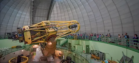 Visitors view a large telescope inside an observatory dome.