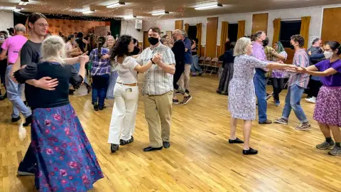 People dancing in a community hall with a wooden floor.