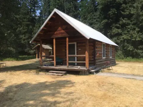 A wooden cabin sits surrounded by trees and dry grass.
