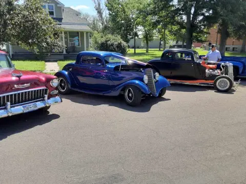 Classic cars parked on an asphalt street with a house in the background.