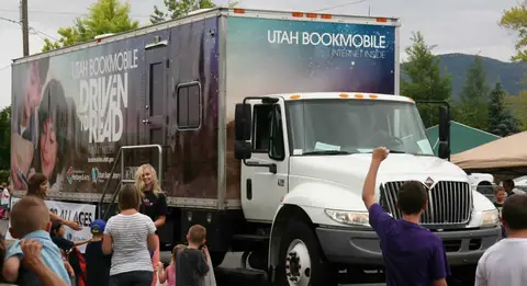 A large bookmobile truck parked outside with people gathered around it.