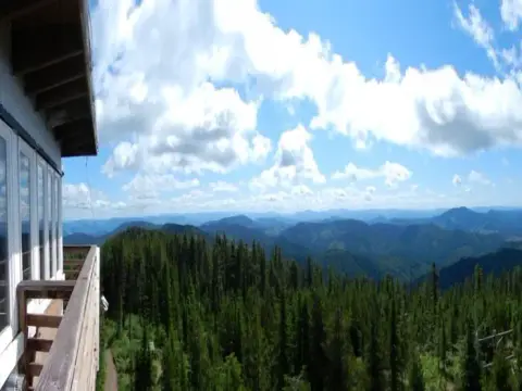 A view of forested mountains and a cloudy blue sky from a lookout tower balcony.