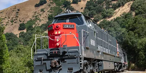 A locomotive on tracks against a hillside backdrop.