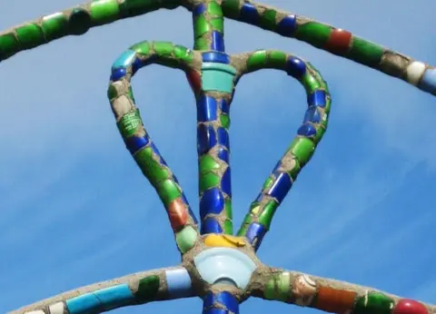 A close-up of a mosaic structure decorated with colorful pieces of glass against a blue sky.