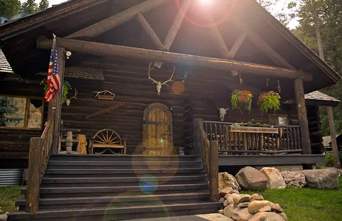 A log cabin exterior with a front porch, stairs, and decorative items.